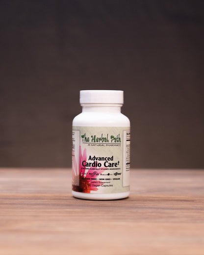 A white bottle of The Herbal Park Organic Chaga supplement stands centered on a wooden tabletop, with blurred herbal props on both sides against a dark backdrop.