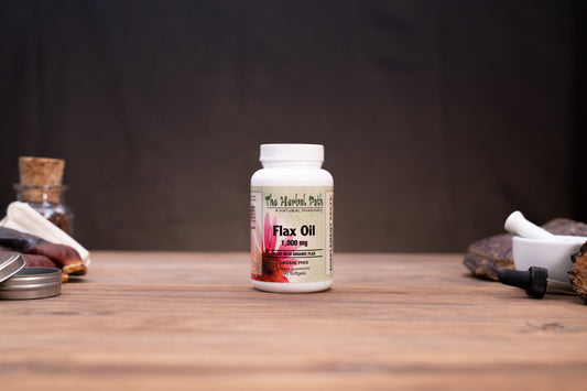 A white bottle of The Herbs Patch Flax Oil 3,000 mg centered on a wooden tabletop, with blurred herbal props in the background.