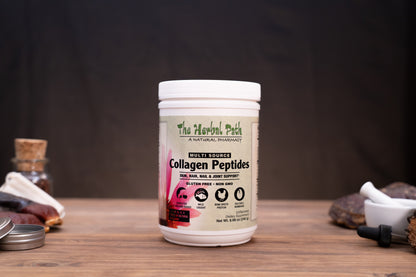 A white plastic tub of The Herbal Path Collagen Peptides centered on a wooden table, with a dark draped backdrop behind it and small rustic props on both sides.