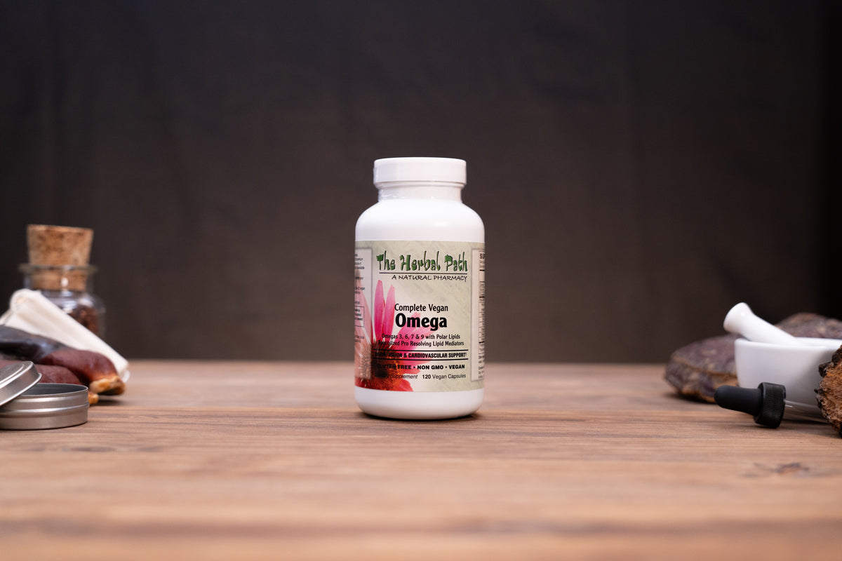 A white bottle of The Herbal Patch Omega dietary supplement standing on a wooden tabletop, with blurred herbal props in the background.