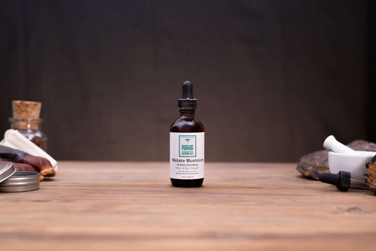A small amber glass dropper bottle labeled 'Fungi Forest' and 'Bofra Mushroom' stands centered on a wooden tabletop against a dark backdrop, with rustic props softly blurred at the sides.