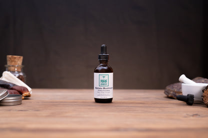 A small amber glass dropper bottle labeled 'Fungi Forest' and 'Bofra Mushroom' stands centered on a wooden tabletop against a dark backdrop, with rustic props softly blurred at the sides.