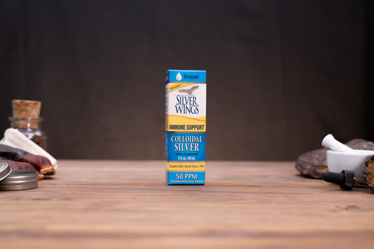 Silver Wings Colloidal Silver 50 PPM liquid supplement box standing on a wooden tabletop with rustic props blurred in the background.