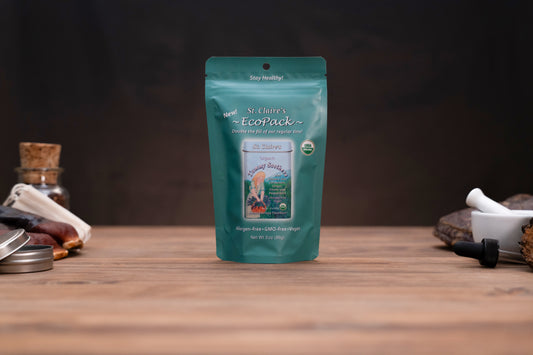 A teal stand-up pouch of St. John's Wort herbal supplement centered on a wooden tabletop, with small kitchen or herbal-prep props visible on both sides against a dark background.