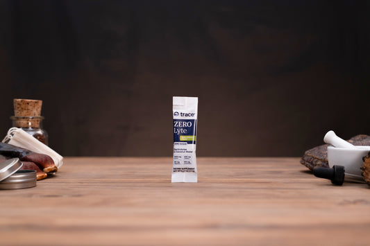 A single tube of trace Zero Laryngitis throat relief spray stands upright on a wooden tabletop against a dark, moody background. The tube is white with black and yellow text.