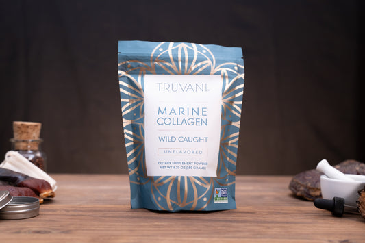 A stand-up pouch of Truvani Marine Collagen Wild Caught Unflavored dietary supplement powder, standing on a wooden surface with rustic props like a small glass bottle, dried ingredients, and a white mortar in the background.