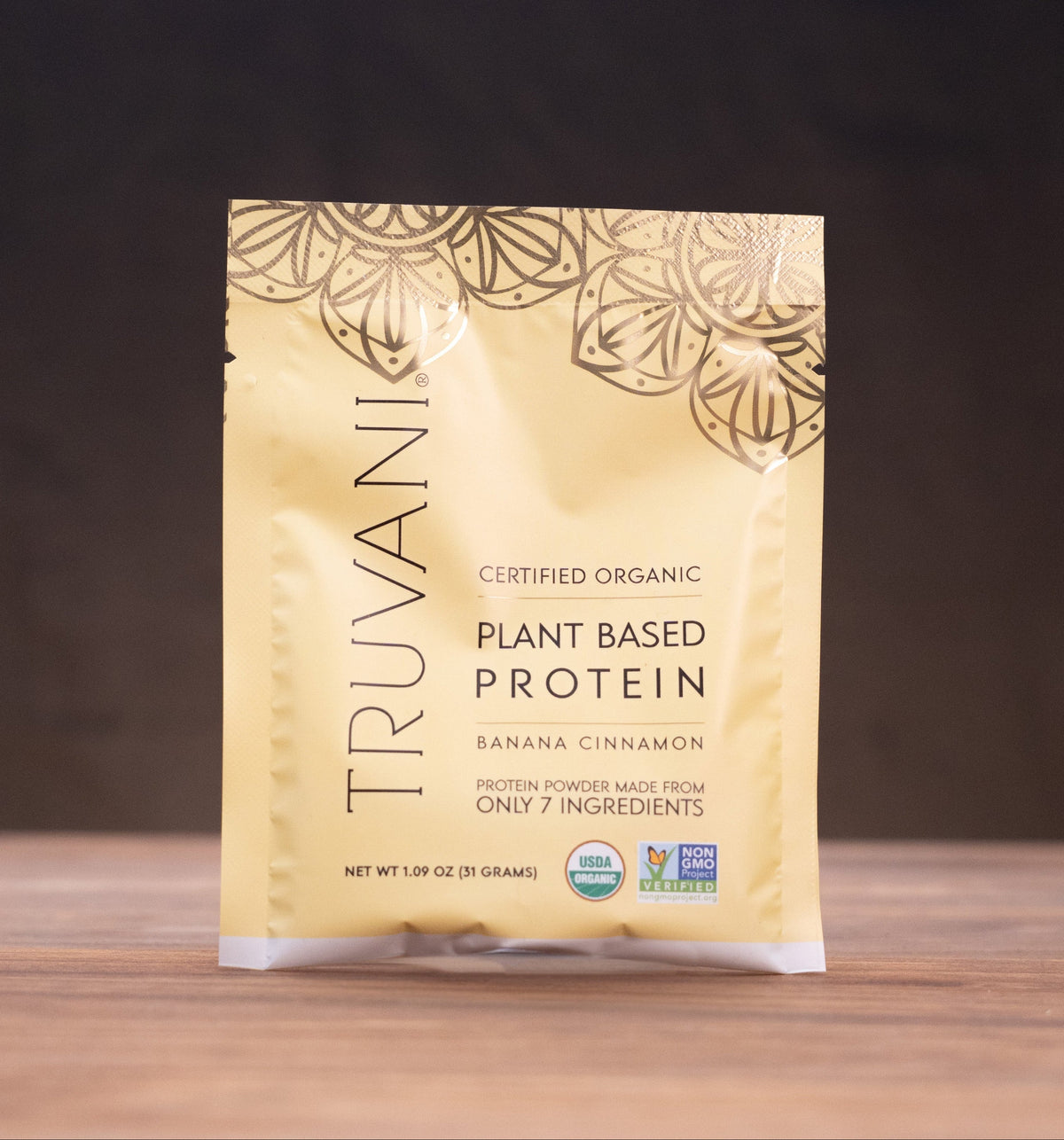 A pouch of Truvanic Certified Organic Plant Based Protein in Banana Cinnamon flavor, standing on a wooden surface with rustic props in the background.