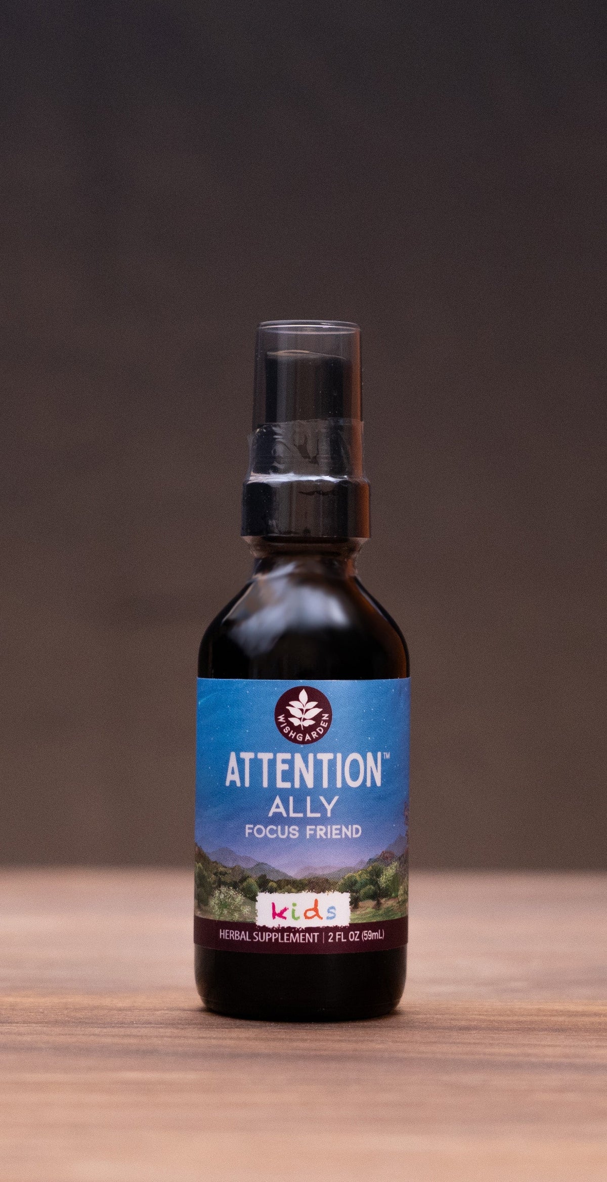 A small amber glass bottle labeled ATTENTION KILL centered on a wooden tabletop, with blurred natural props and a dark backdrop around it.